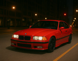 A red BMW E36 M3 driving through the city at night with AKG performance parts.