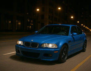 A blue BMW E46 M3 driving through the city at night with AKG performance parts.
