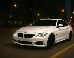 A white BMW F32 driving through the city at night with AKG performance parts.